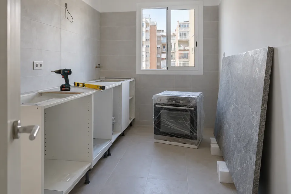 Muebles de cocina a medio montar y encimera apoyada en la pared durante la reforma de un piso