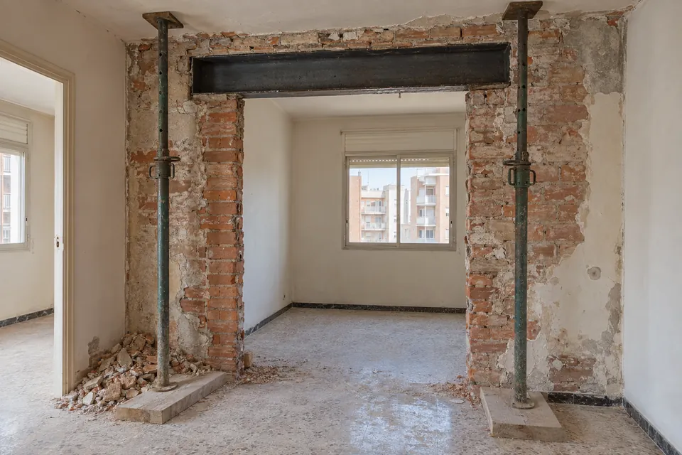 Hueco recién abierto en un muro de ladrillo macizo con una viga metálica y puntales en un piso en obras