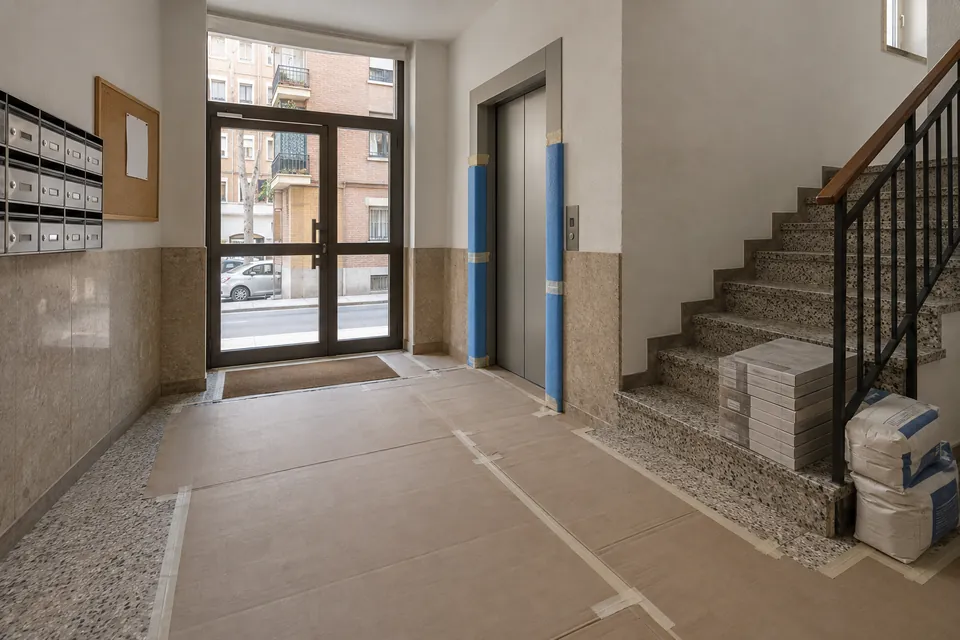 Portal de un bloque de pisos con el suelo protegido con cartón y cajas de material antes de una obra