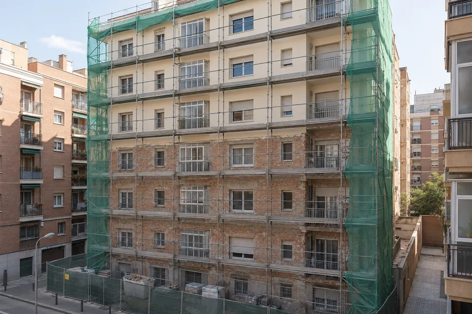 Fachada de un bloque de los años 60 con andamio y malla durante su rehabilitación