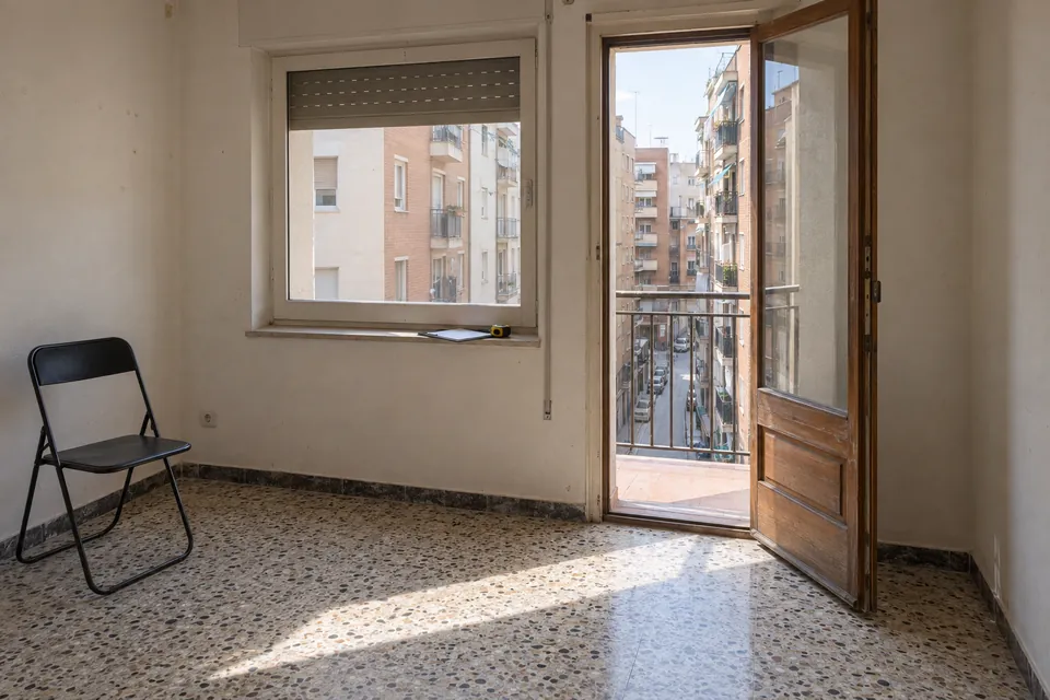 Salón vacío de un piso antiguo con suelo de terrazo, preparado para la visita de presupuesto
